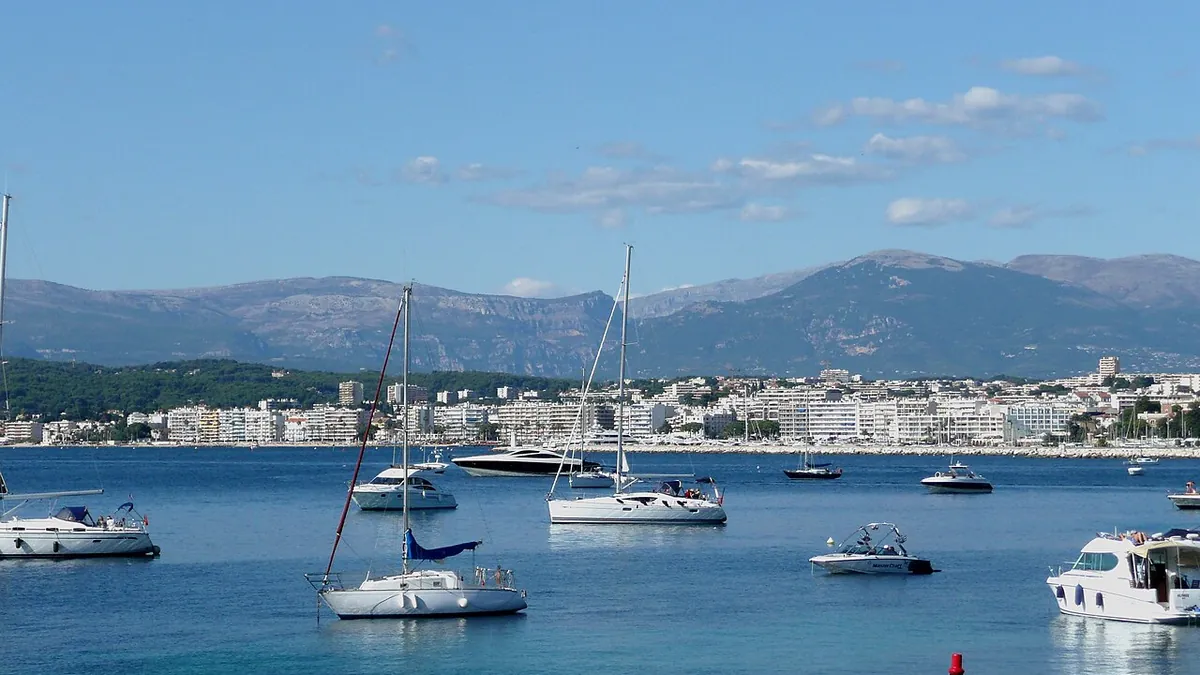 La baie de Juan-les-Pins vue depuis le Cap d'Antibes, voiliers au mouillage et montagnes en arrière-plan